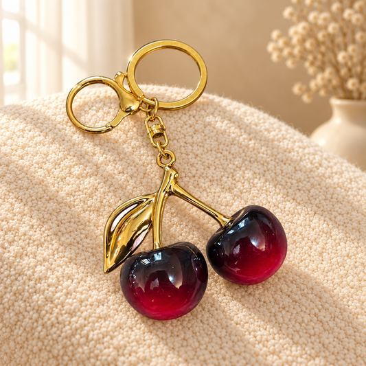 Burgundy cherry keychain with gold hardware on cream boucle in warm sunlight